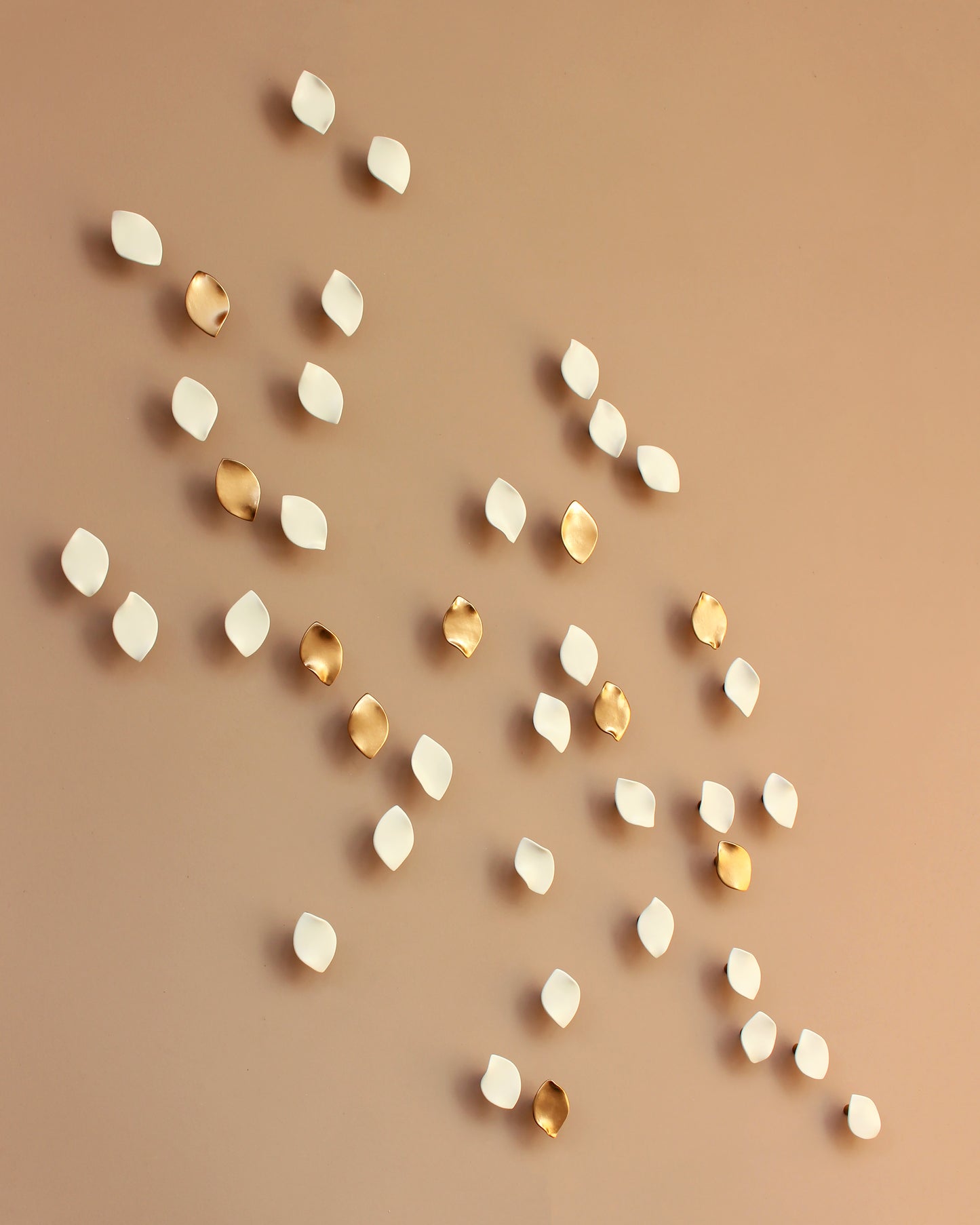 Gold and white decorative elements on a beige background. Porcelain petals, flower petals wall art, leaf like shape - they float in front of the wall