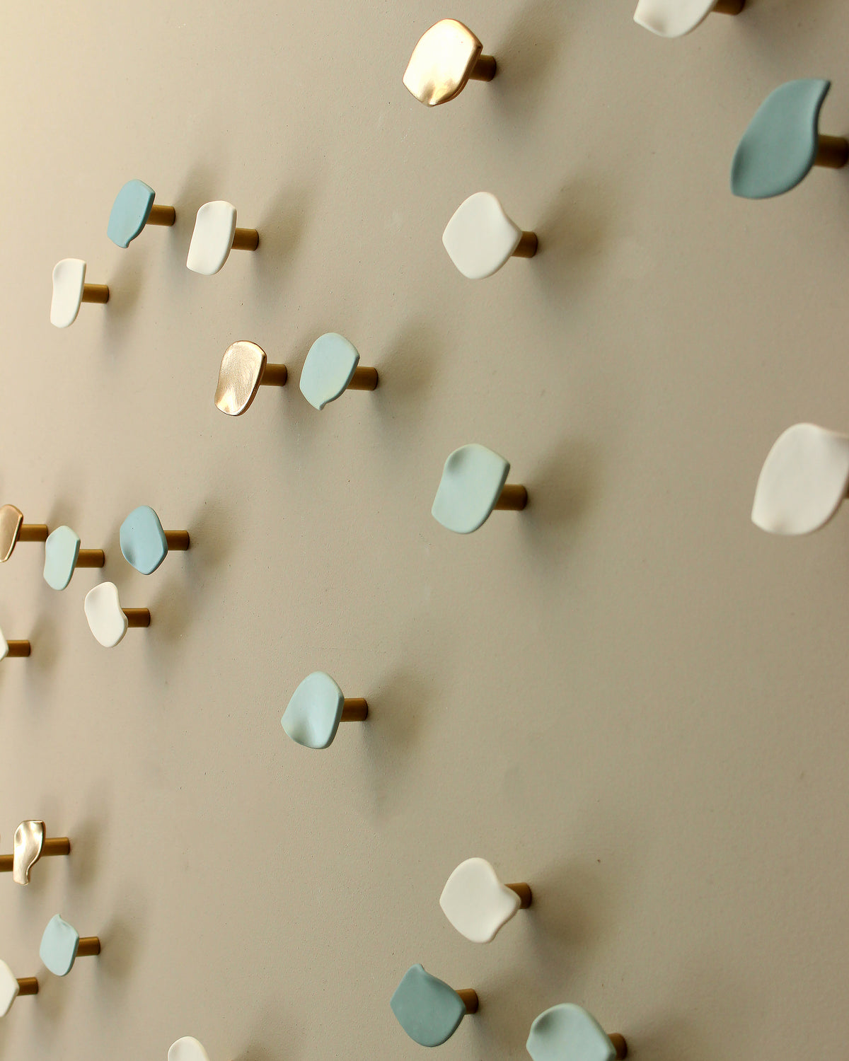 A close-up of a wall-mounted decorative arrangement of small ceramic wall sculptures making an art installation in white, light blue, and metallic gold on a beige wall.