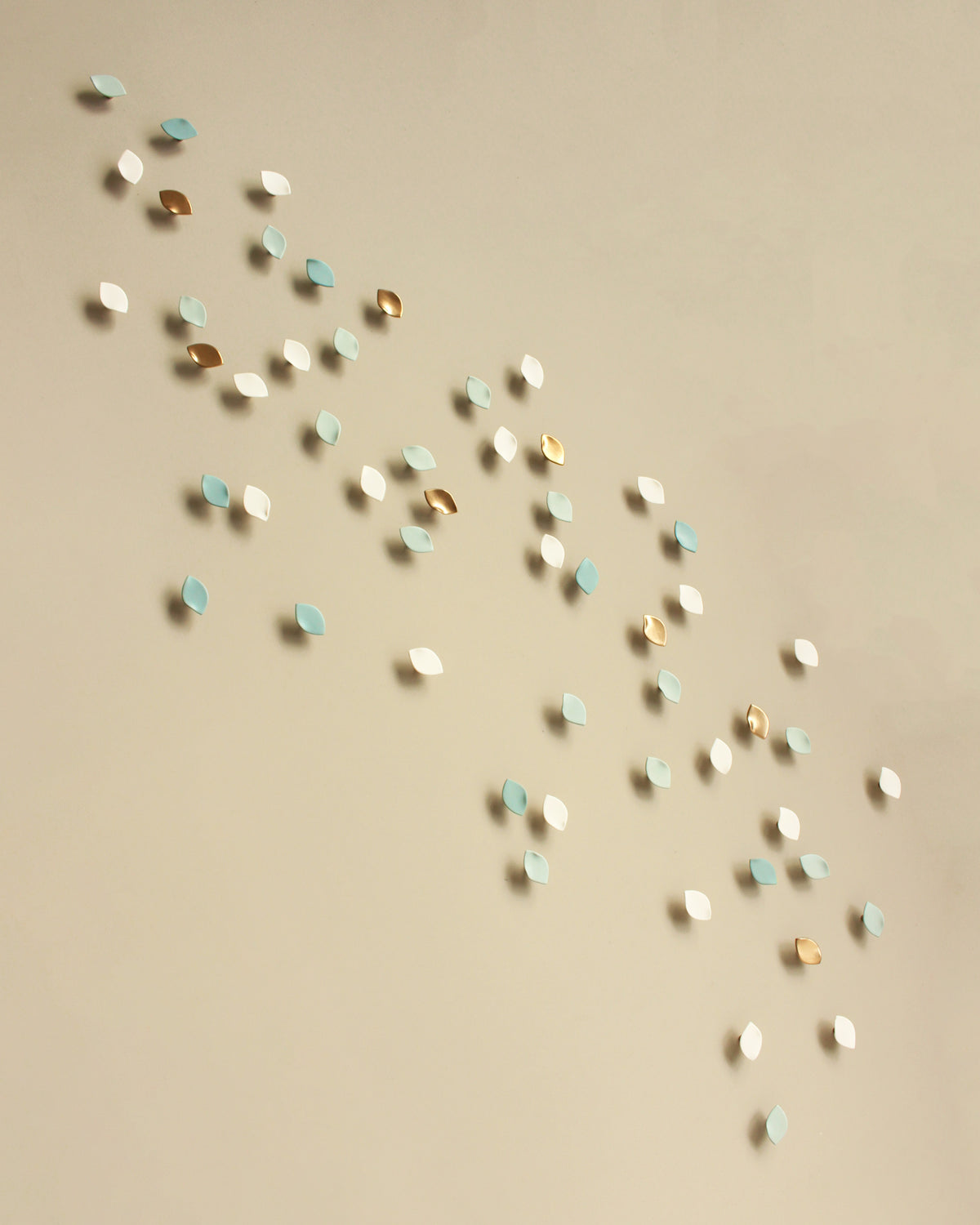 Small scattered decorative wall art pieces in white, light blue, and metallic gold arranged diagonally on a warm beige background to create a large wall art installation. Luxury handmade wall art
