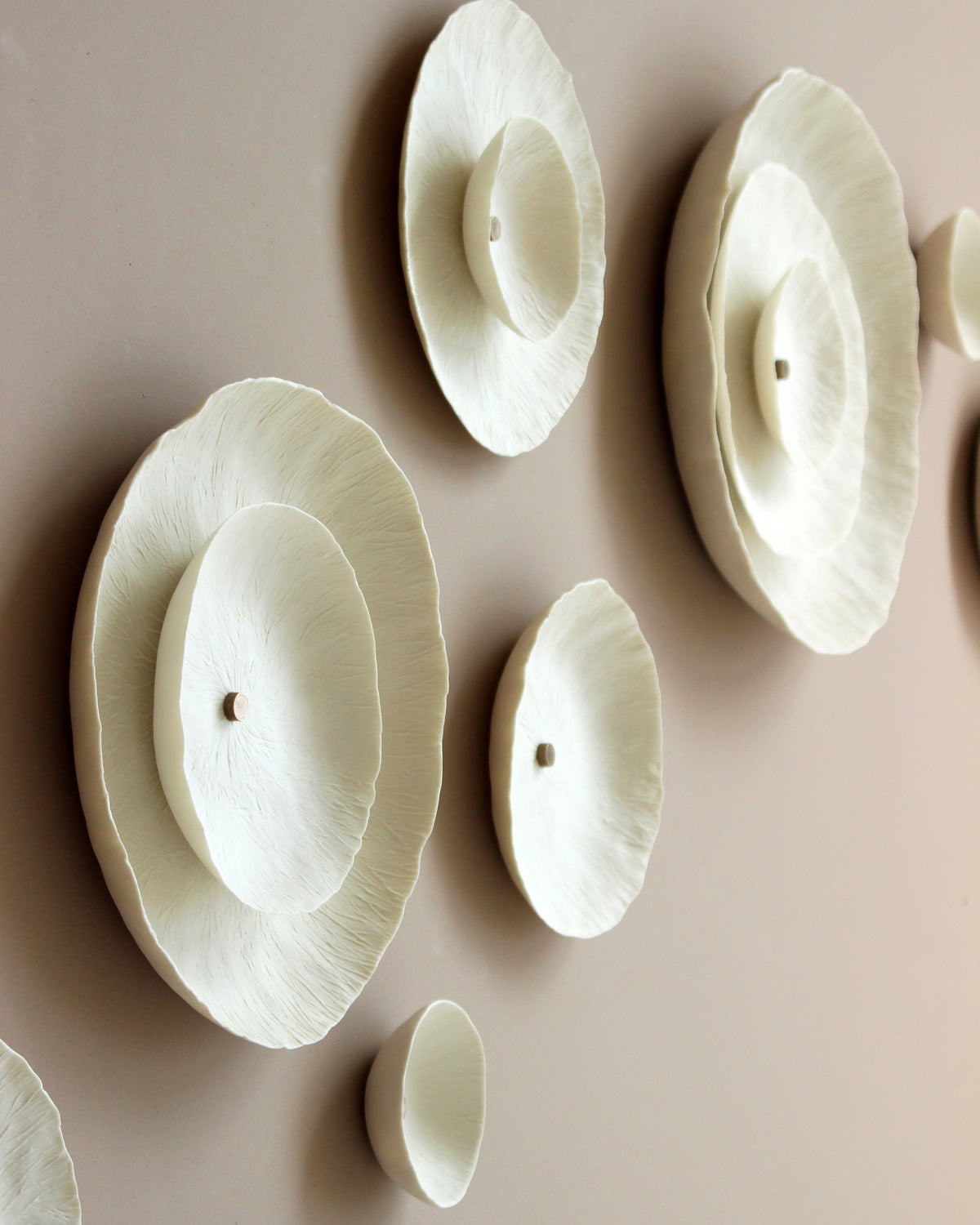 White ceramic circular shaped wall decor mounted on a warm beige wall. Each piece has a gold stud in the centre.