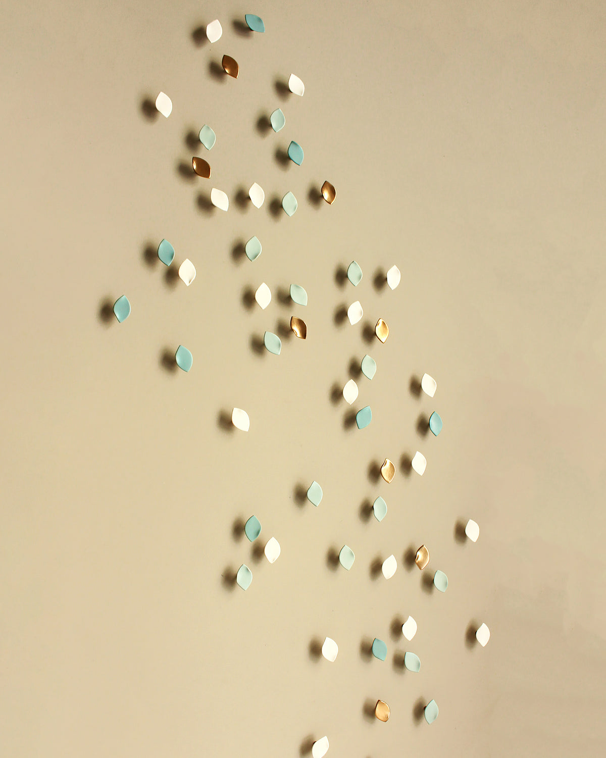 Small decorative wall sculpture in white, light blue, and metallic gold scattered on a plain beige wall.