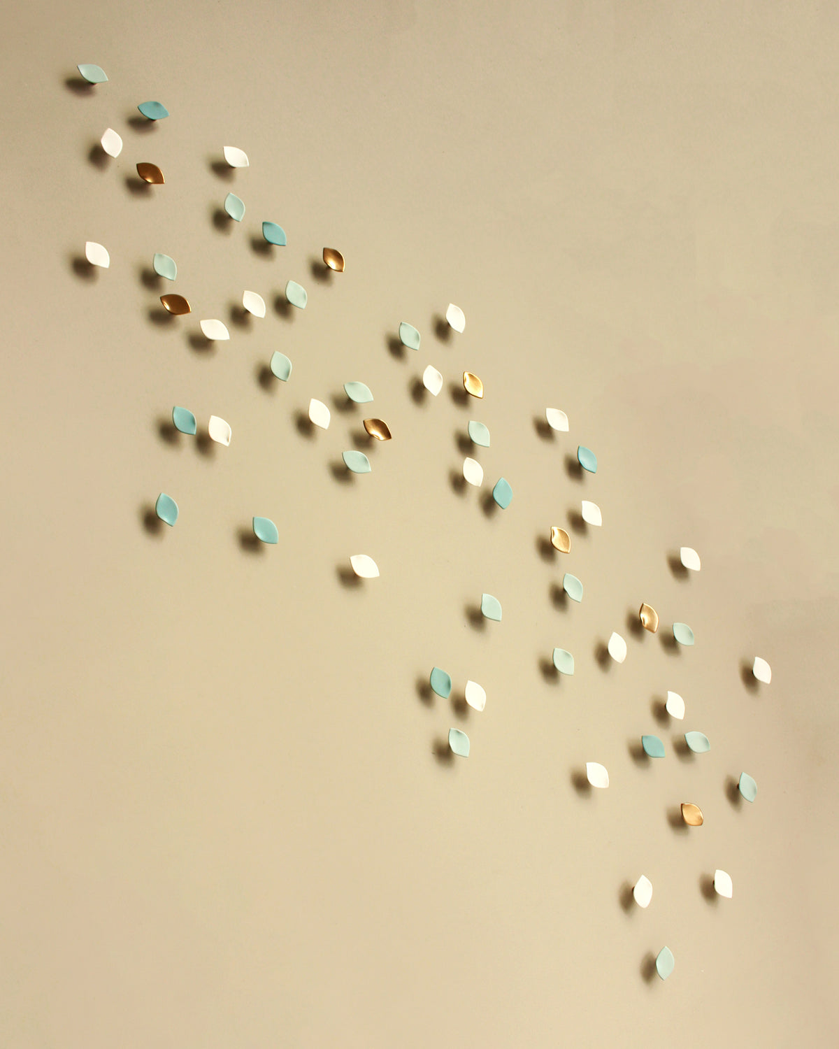 Small scattered decorative wall art pieces in white, light blue, and metallic gold arranged diagonally on a warm beige background.