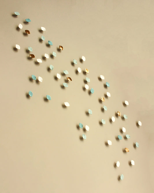 Small scattered decorative wall art pieces in white, light blue, and metallic gold arranged diagonally on a warm beige background.